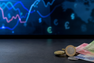 Monedas y billetes mexicanos junto a una pantalla con referencias cambiarias