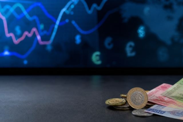 Monedas y billetes mexicanos junto a una pantalla con referencias cambiarias