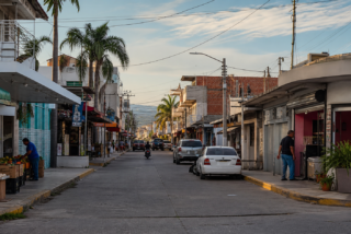 Calle comercial de Sinaloa con negocios abiertos y tránsito moderado, en una escena de economía local bajo vigilancia.
