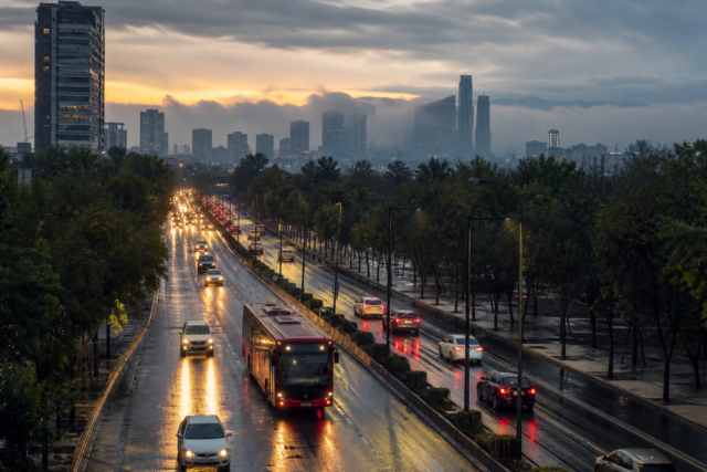 Avenida de Ciudad de México con tráfico matutino y pavimento mojado bajo cielo nublado