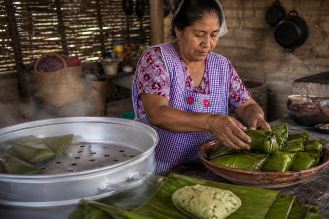 Cocinera tradicional acomoda tamales de chipilín envueltos en hojas dentro de una vaporera.