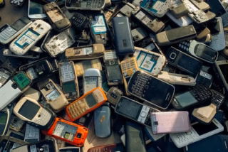 Teléfono celular y pequeños aparatos electrónicos separados sobre una mesa, imagen ilustrativa para una guía de reutilización y reciclaje.