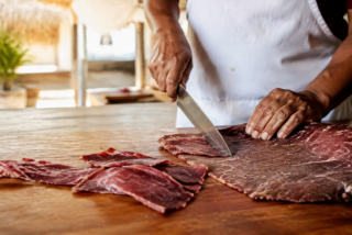 Maestro tasajeador corta cecina artesanal de Yecapixtla sobre una mesa de madera