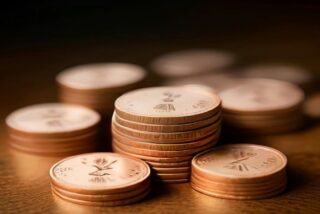 Pilas ordenadas de monedas cobrizas sobre una mesa de madera oscura con luz cálida y fondo desenfocado, sin personas ni texto