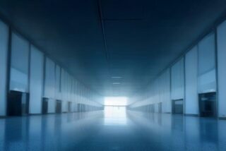 Pasillo largo y vacío de una terminal con muros de cristal, iluminación azul y piso pulido que refleja la luz