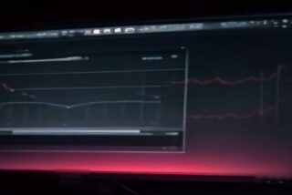 Monitor de computadora en una habitación oscura con líneas rojas de una gráfica financiera que brillan sobre la pantalla