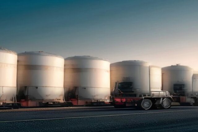 Pipas de combustible estacionadas frente a grandes tanques cilíndricos blancos de una terminal de almacenamiento al atardecer