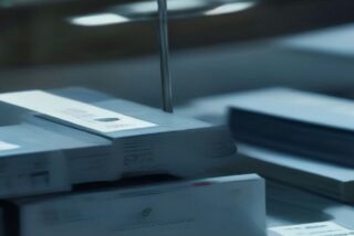 Pilas de tarjetas plásticas en blanco y sobres sobre una mesa industrial con luz fría y fondo desenfocado