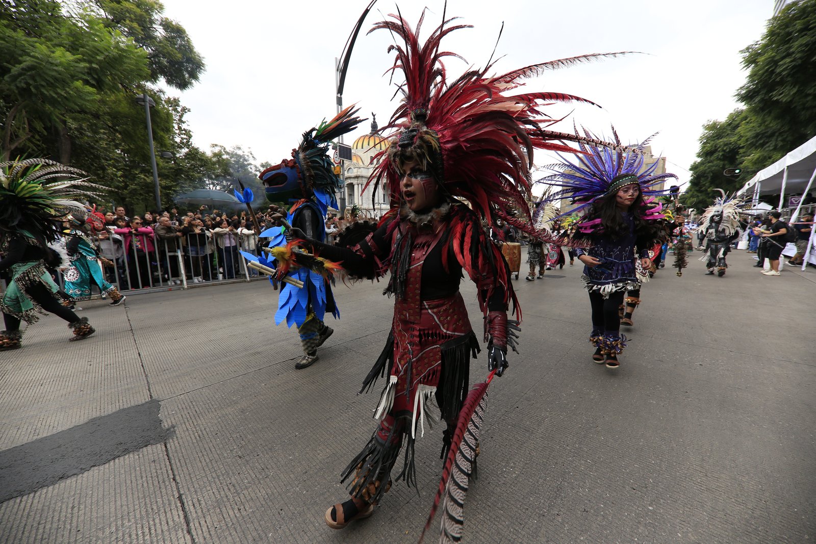 Danzantes con penachos de plumas participan en el Desfile de Alebrijes Monumentales con el Palacio de Bellas Artes al fondo