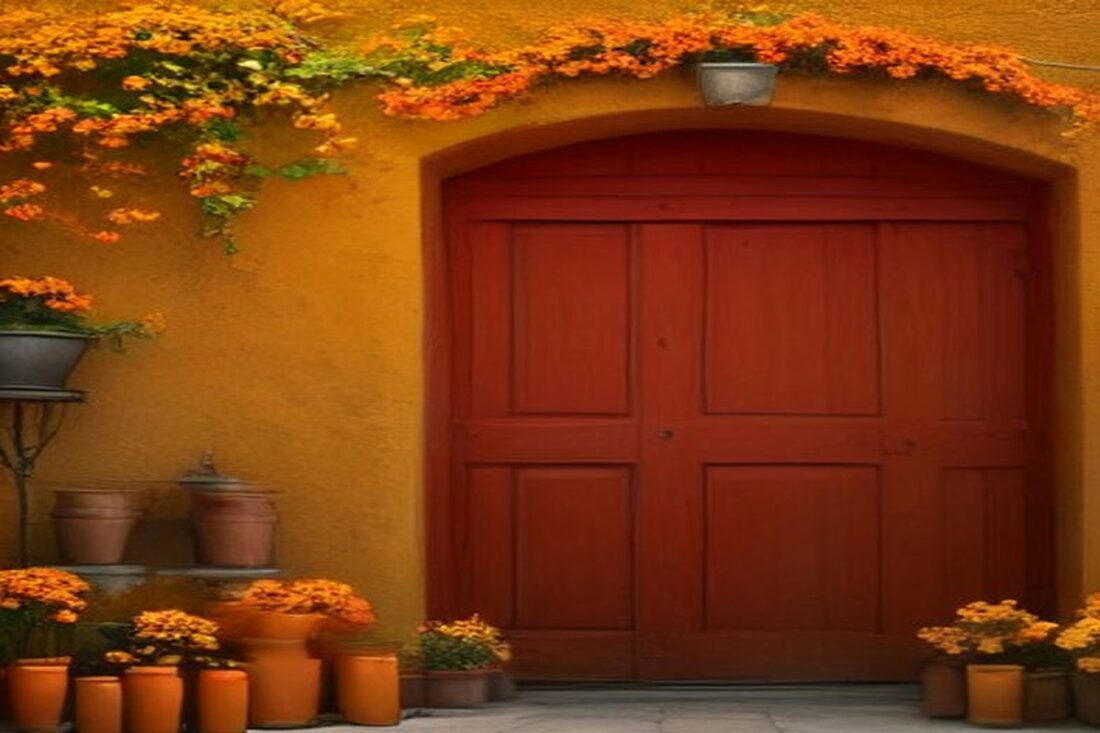Fachada colonial de muro ocre con puerta de madera roja, macetas de barro y flores de cempasúchil sobre el arco, alusiva al Día de Muertos en Oaxaca 2026
