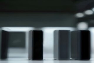 Varios dispositivos oscuros alineados sobre una mesa blanca de exhibición en una tienda iluminada