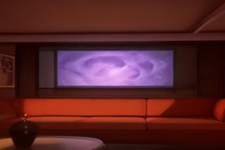 Sala en penumbra con un sillón naranja frente a una pantalla que proyecta un resplandor cósmico morado, alusiva al estreno de Dragon Ball Super: Beerus en streaming