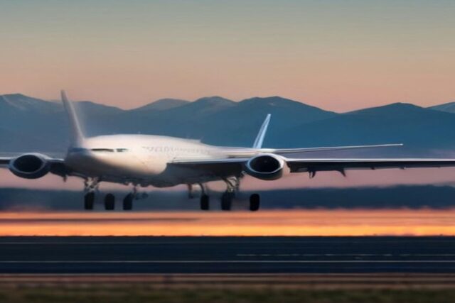 Avión de pasajeros blanco sin insignias en una pista de aeropuerto al amanecer con montañas al fondo