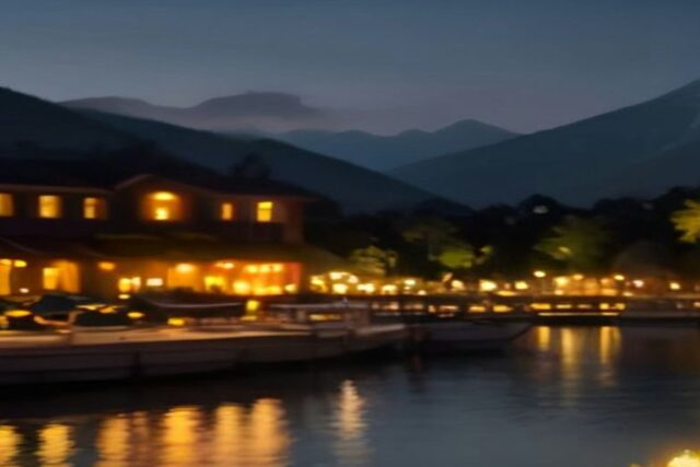 Pueblo a la orilla de un lago de noche con edificios, muelle y lanchas iluminados con luz cálida y montañas al fondo, alusivo a la cartelera del Festival de las Almas 2026 en Valle de Bravo