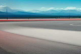 Pista de carreras vacía con una curva de asfalto, borde rojo y montañas al fondo bajo un cielo azul, alusiva al Gran Premio de México 2026