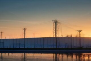 Torres de alta tensión y una nave industrial al atardecer reflejadas en el agua, alusivas a la inversión privada en energía e industria en México