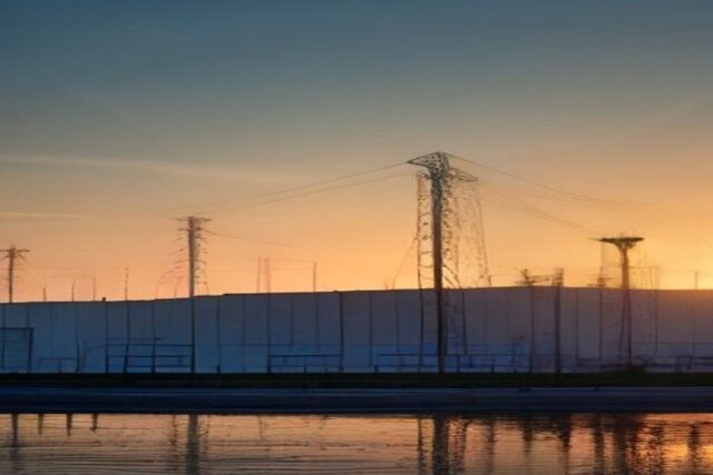 Torres de alta tensión y una nave industrial al atardecer reflejadas en el agua, alusivas a la inversión privada en energía e industria en México