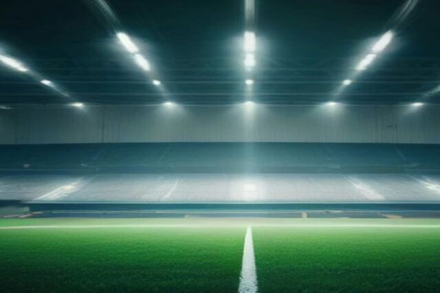 Estadio de futbol vacío de noche con reflectores encendidos sobre el césped verde y la línea central blanca, alusivo a la Jornada 15 de la Liga MX Apertura 2026