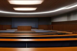 Recinto legislativo vacío con filas de escritorios de madera y luces en el techo, sin personas ni texto