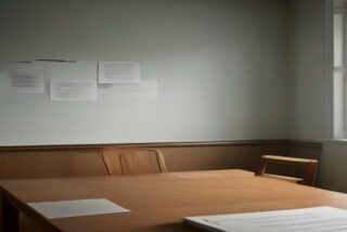 Sala de reuniones vacía con una mesa de madera, sillas, hojas sobre la mesa y papeles fijados en la pared, iluminada por una ventana