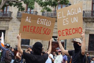 Manifestantes sostienen pancartas con las frases "Al estilo Mierdisco" y "El agua es un derecho" frente a Palacio de Gobierno de Jalisco durante la marcha Agua Limpia