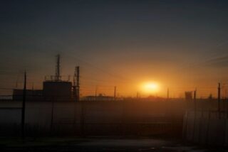 Cerca perimetral con alambre de púas de una instalación petrolera al anochecer, con chimeneas y estructuras industriales a contraluz, alusiva al ataque en un acceso de la refinería de Minatitlán
