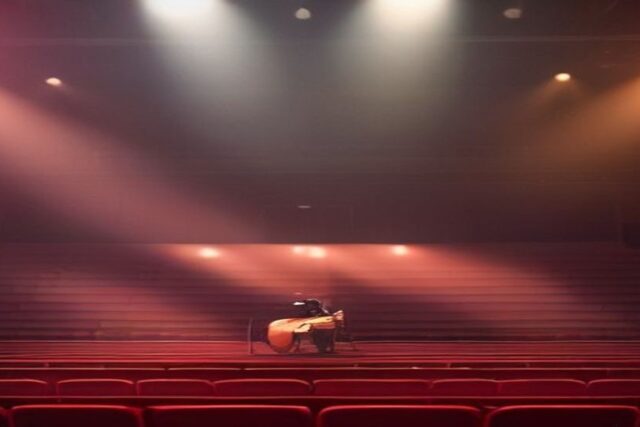 Escenario de arena vacío con una guitarra acústica bajo reflectores rosas y ámbar entre bruma y butacas rojas vacías, alusivo a los conciertos de Niall Horan en México 2027