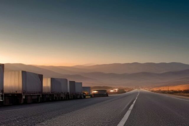 Carretera vacía al amanecer entre montañas con una fila de tractocamiones de caja blanca estacionados a un costado del camino, alusiva al paro de transportistas del 26 de octubre