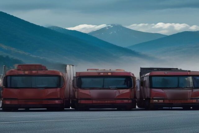 Fila de tractocamiones rojos detenidos uno junto a otro en una explanada, con montañas y nubes al fondo