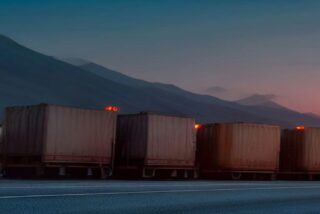 Fila de camiones de carga estacionados a la orilla de una carretera al atardecer con montañas al fondo