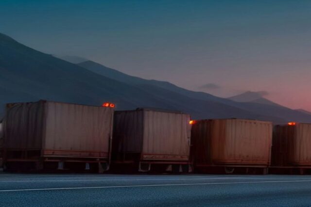 Fila de camiones de carga estacionados a la orilla de una carretera al atardecer con montañas al fondo