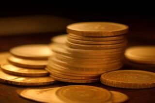Pilas de monedas doradas sobre una superficie de madera con luz cálida y fondo oscuro desenfocado