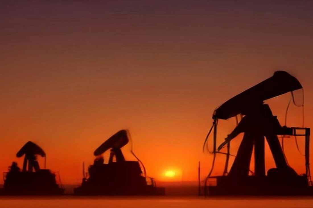 Siluetas de varias bombas extractoras de petróleo en un campo petrolero al atardecer, con el cielo naranja y el sol en el horizonte