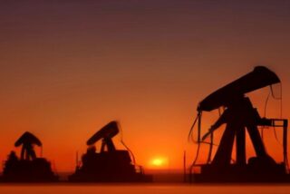 Siluetas de varias bombas extractoras de petróleo en un campo petrolero al atardecer, con el cielo naranja y el sol en el horizonte
