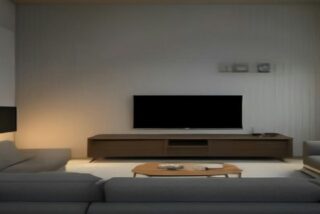 Sala moderna con una televisión apagada sobre un mueble de madera, sillones grises y mesa de centro con luz cálida, alusiva a los precios de streaming en México 2026