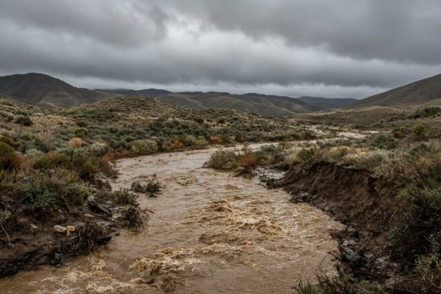 Arroyo crecido entre lomeríos bajo cielo nublado con vegetación mojada, alusivo a las comunidades incomunicadas por la tormenta Rachel