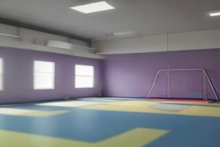 Sala de terapia vacía con piso de colores, paredes lilas, ventanas y un aparato de ejercicio al fondo