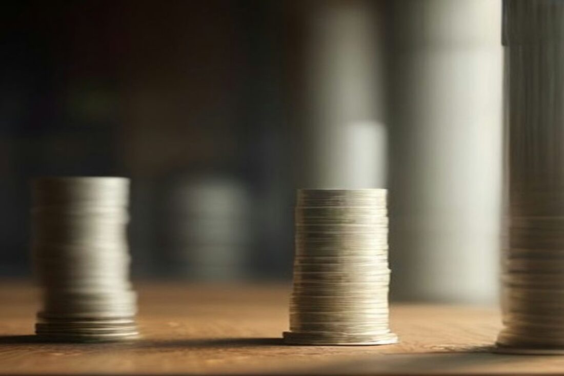 Columnas de monedas apiladas que crecen de izquierda a derecha sobre un escritorio de madera, alusivas al salario mínimo 2027
