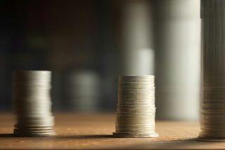 Columnas de monedas apiladas que crecen de izquierda a derecha sobre un escritorio de madera, alusivas al salario mínimo 2027