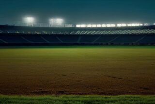 Estadio de beisbol vacío de noche con reflectores encendidos, pasto verde y el diamante de tierra iluminado
