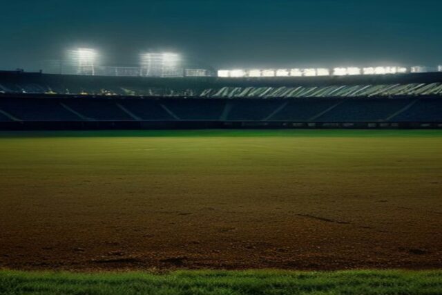 Estadio de beisbol vacío de noche con reflectores encendidos, pasto verde y el diamante de tierra iluminado