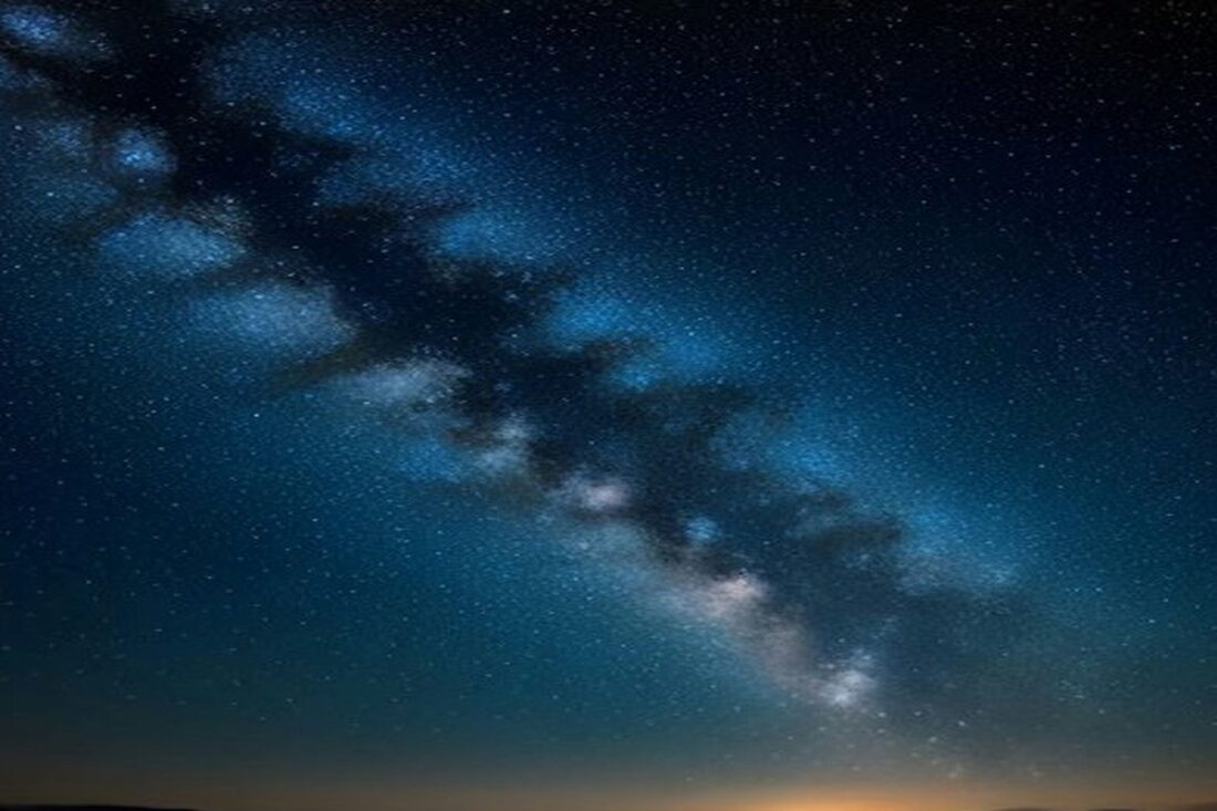 Cielo nocturno lleno de estrellas con la Vía Láctea en diagonal y un trazo de meteoro sobre un horizonte oscuro, alusivo a la lluvia de estrellas Táuridas 2026
