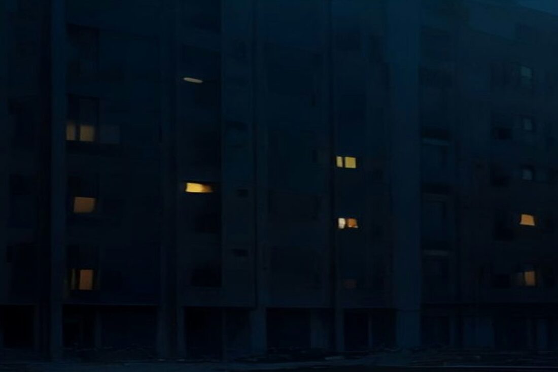 Edificio de departamentos de una ciudad de Europa del Este de noche durante un apagón, con la mayoría de las ventanas a oscuras y solo unas pocas iluminadas, sin personas ni texto