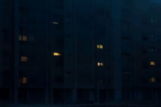 Edificio de departamentos de una ciudad de Europa del Este de noche durante un apagón, con la mayoría de las ventanas a oscuras y solo unas pocas iluminadas, sin personas ni texto