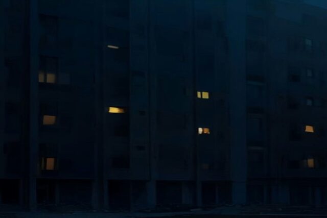 Edificio de departamentos de una ciudad de Europa del Este de noche durante un apagón, con la mayoría de las ventanas a oscuras y solo unas pocas iluminadas, sin personas ni texto