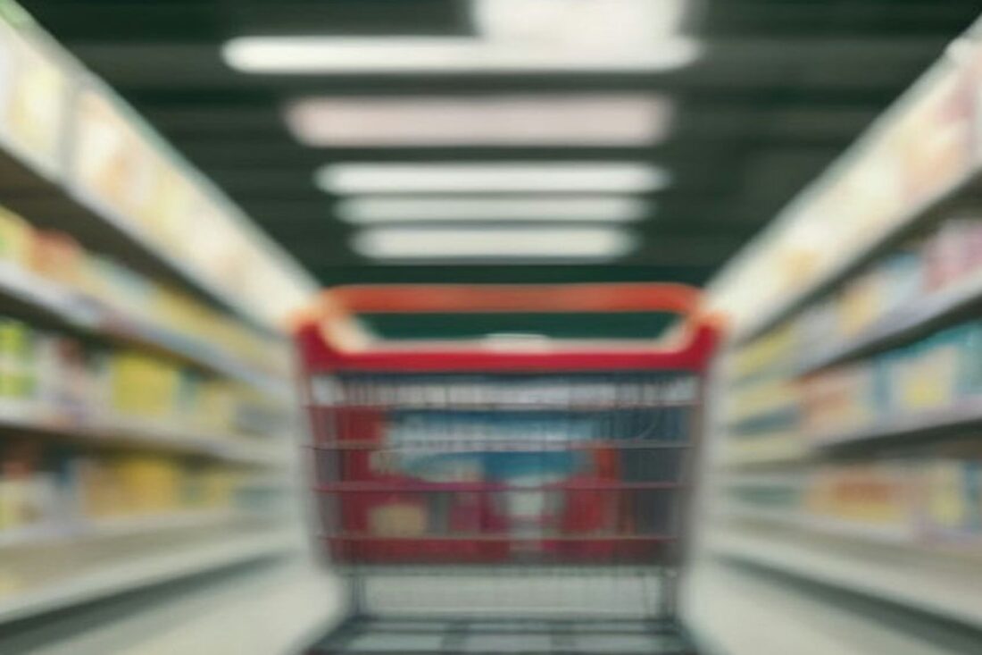 Carrito de supermercado rojo vacío en un pasillo con anaqueles llenos de productos desenfocados
