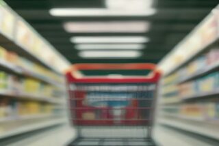 Carrito de supermercado rojo vacío en un pasillo con anaqueles llenos de productos desenfocados